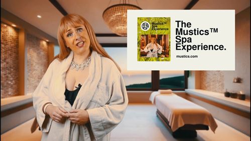 Synergy Myers, a blond white woman in a white dressing gown and diamond necklace, poses quizzically in front of a Spa treatment room. Inset is a card advertising "The Mustics™ Spa Experience" @ mustics.com.